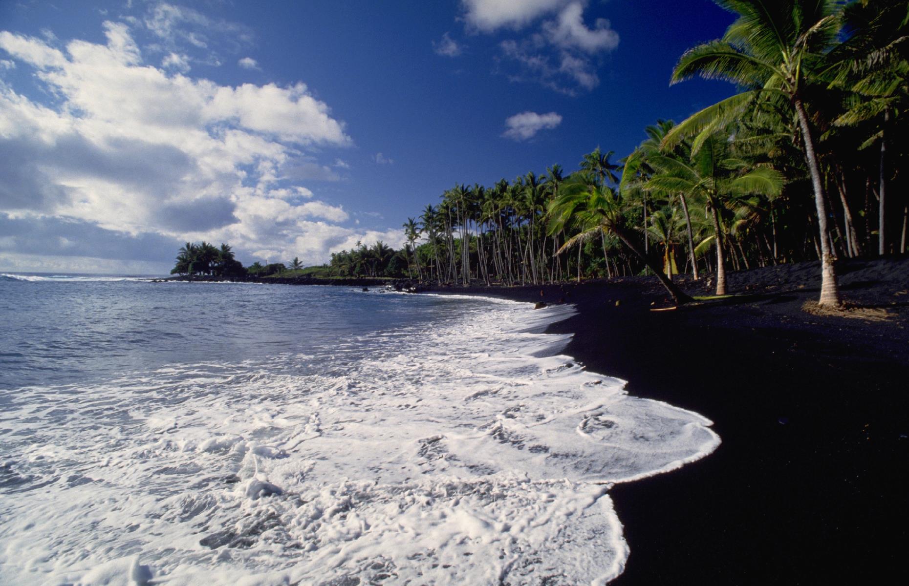 Slide 4 of 31: The Aloha State is known for its stunning black-sand strands and Kaimu Beach, on the Island of Hawaii, was one of the finest. Spreading over an eastern corner of the isle, its inky powder was hemmed in by palms and it drew tourists from across the country. This photo from 1985 shows the beach in all its glory. But, in the 1990s, this natural wonder was destroyed.