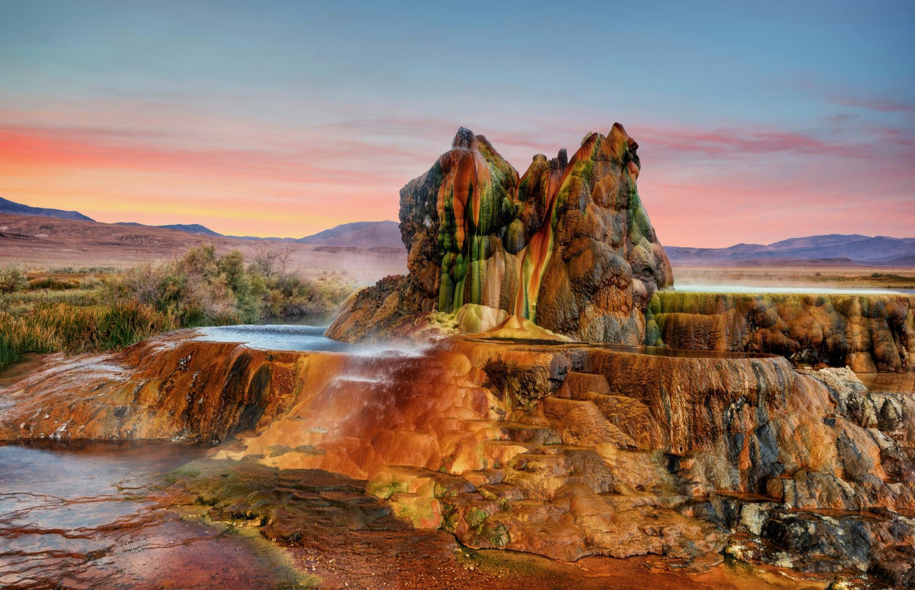 Slide 48 of 59: Over in Nevada's Black Rock Desert, you'll find one of the world's most remarkable geysers. Offering a kaleidoscope of colors and an entirely unique form, Fly Geyser was created by accident. In the 1960s, an energy company drilled on the site in hopes of finding a new power source. The water they found wasn't warm enough but they failed to properly seal the opening they had created. Today, the geyser still spews water and steam, and the brilliant colors are formed by the algae it's covered in.