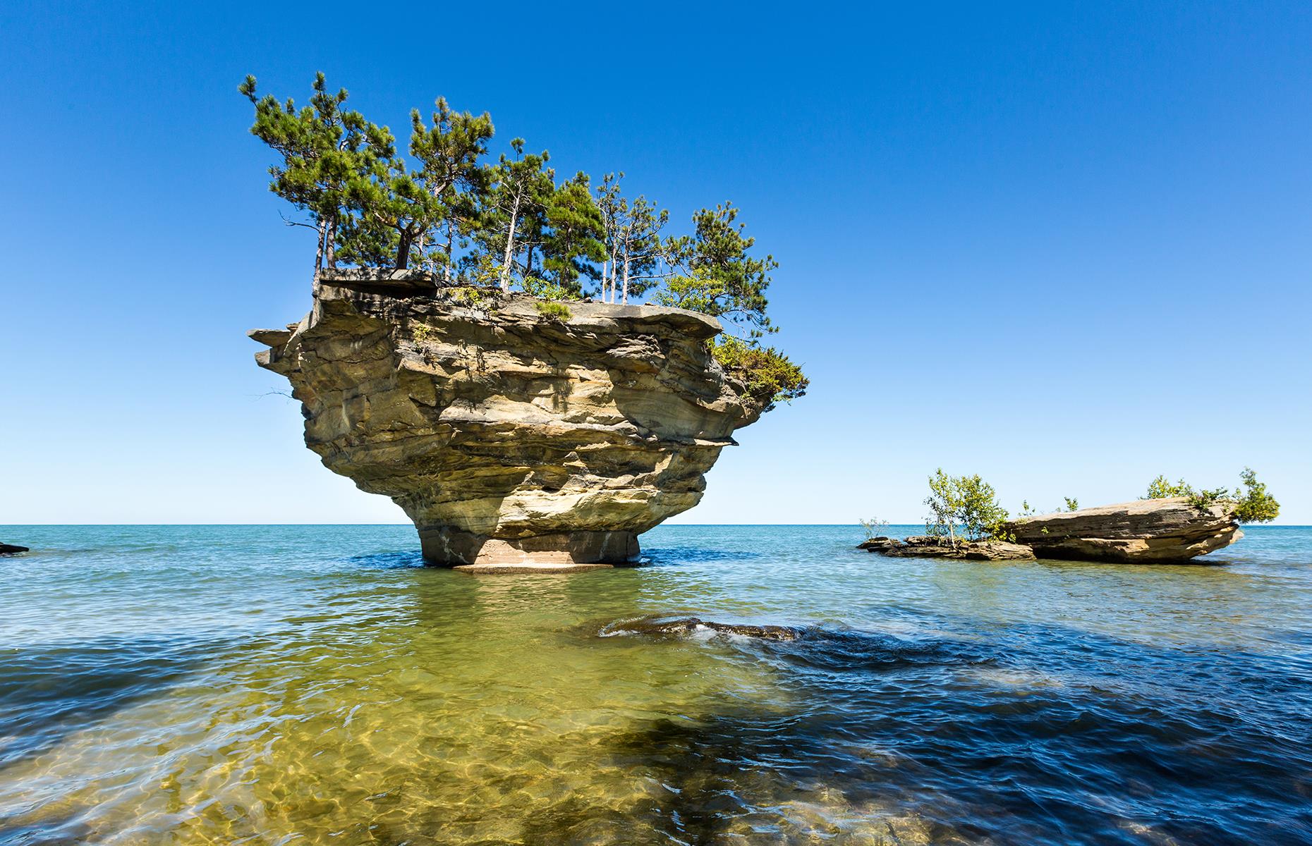 Slide 37 of 41: A small geological formation, Turnip Rock leaves a big impression. Located in shallow waters close to Lake Huron's shore, this peculiar rock took shape due to strong waves crashing against the bottom, causing for some of the lower sections to erode rather significantly. The shallow waters surrounding the rock and the nearby coast are popular kayaking destinations.