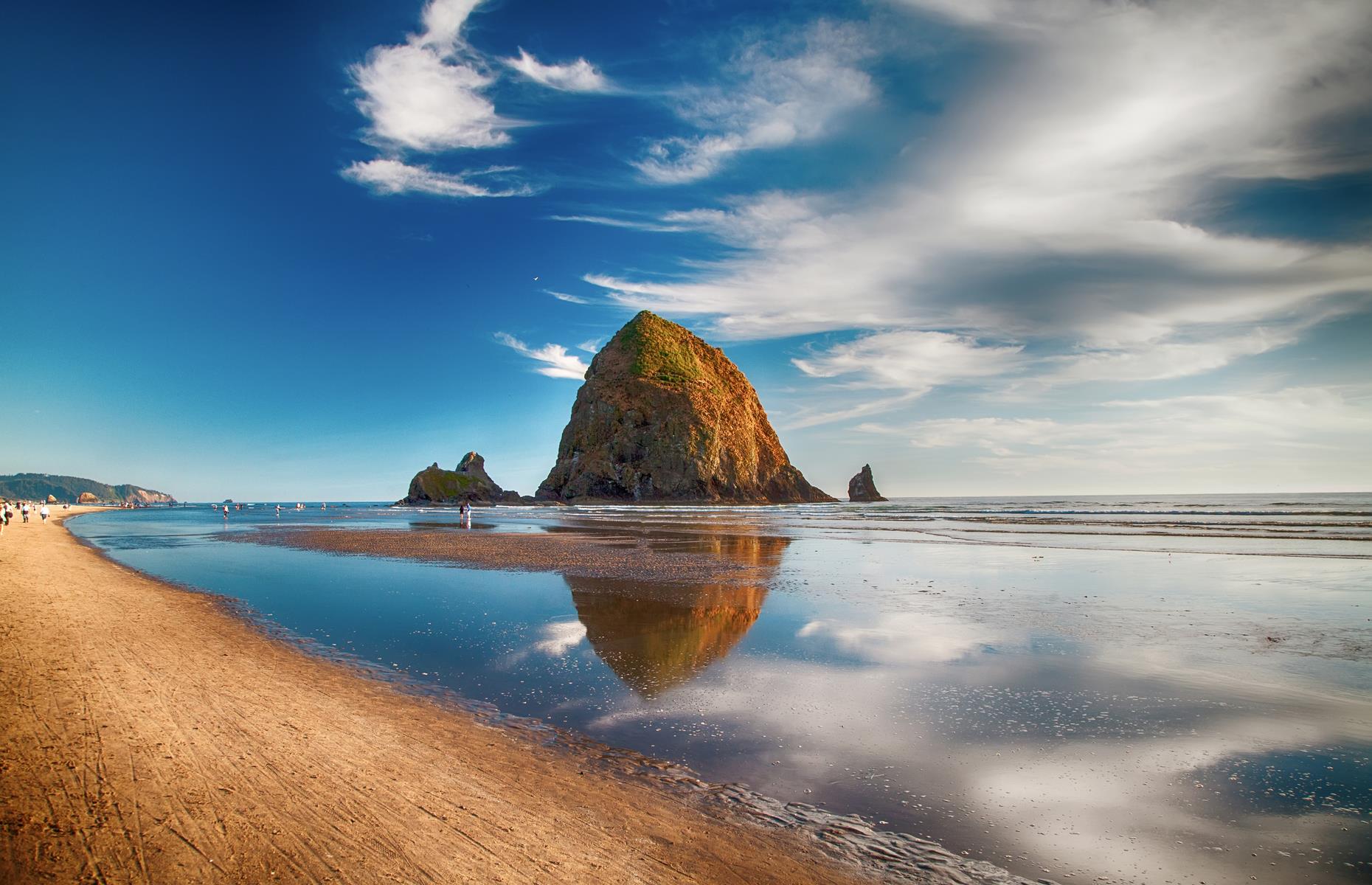 Slide 58 of 100: Oregon's beautiful beaches are often overshadowed by those further south but this strand is one of the most dramatic in the States. It's defined by Haystack Rock, a gigantic sea stack that rises 235 feet (72m) from the Pacific Ocean. In spring and summer, puffins use the rock as a nesting site.