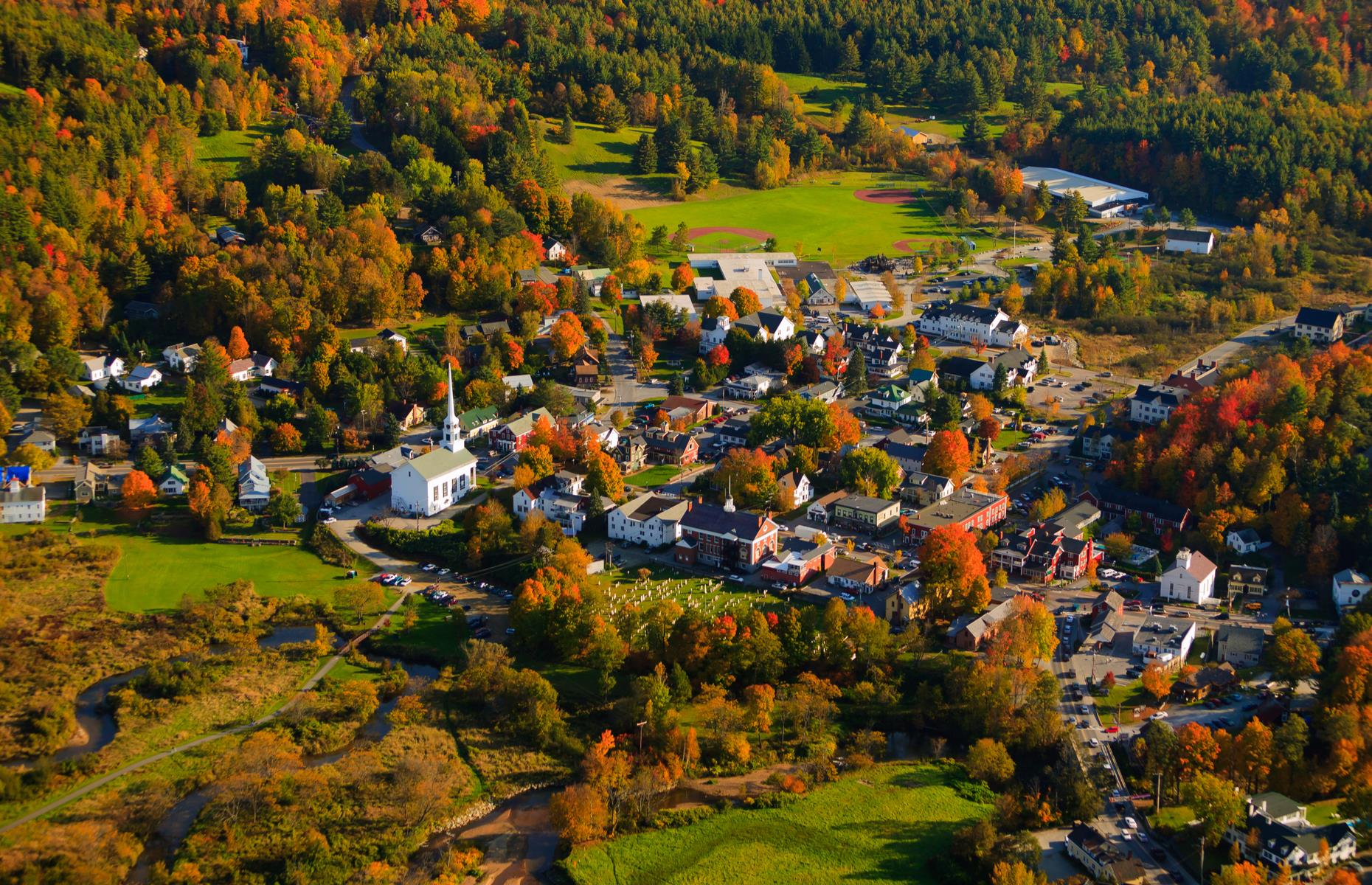 Slide 21 of 45: New England isn't short of quaint small towns that come to life in the fall and one of them is Stowe, a dinky resort town in northern Vermont known for its skiing slopes and walking trails. Its defining feature is the white-washed Stowe Community Church, with its sloping roof and striking steeple. It's seen here surrounded by orange trees as the golden season begins. 