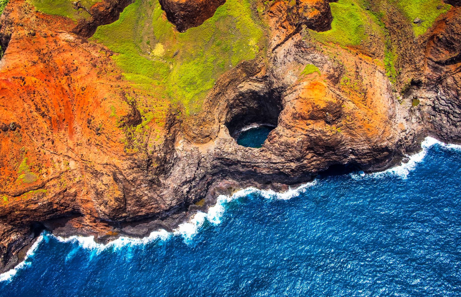 Slide 17 of 45: The otherworldly shores of Nā Pali Coast State Wilderness Park are unlike those anywhere else in the United States. Splashed with popping orange and green, the ridged peaks of Nā Pali, on the island of Kauai, drop down towards sand beaches and a windswept ocean.