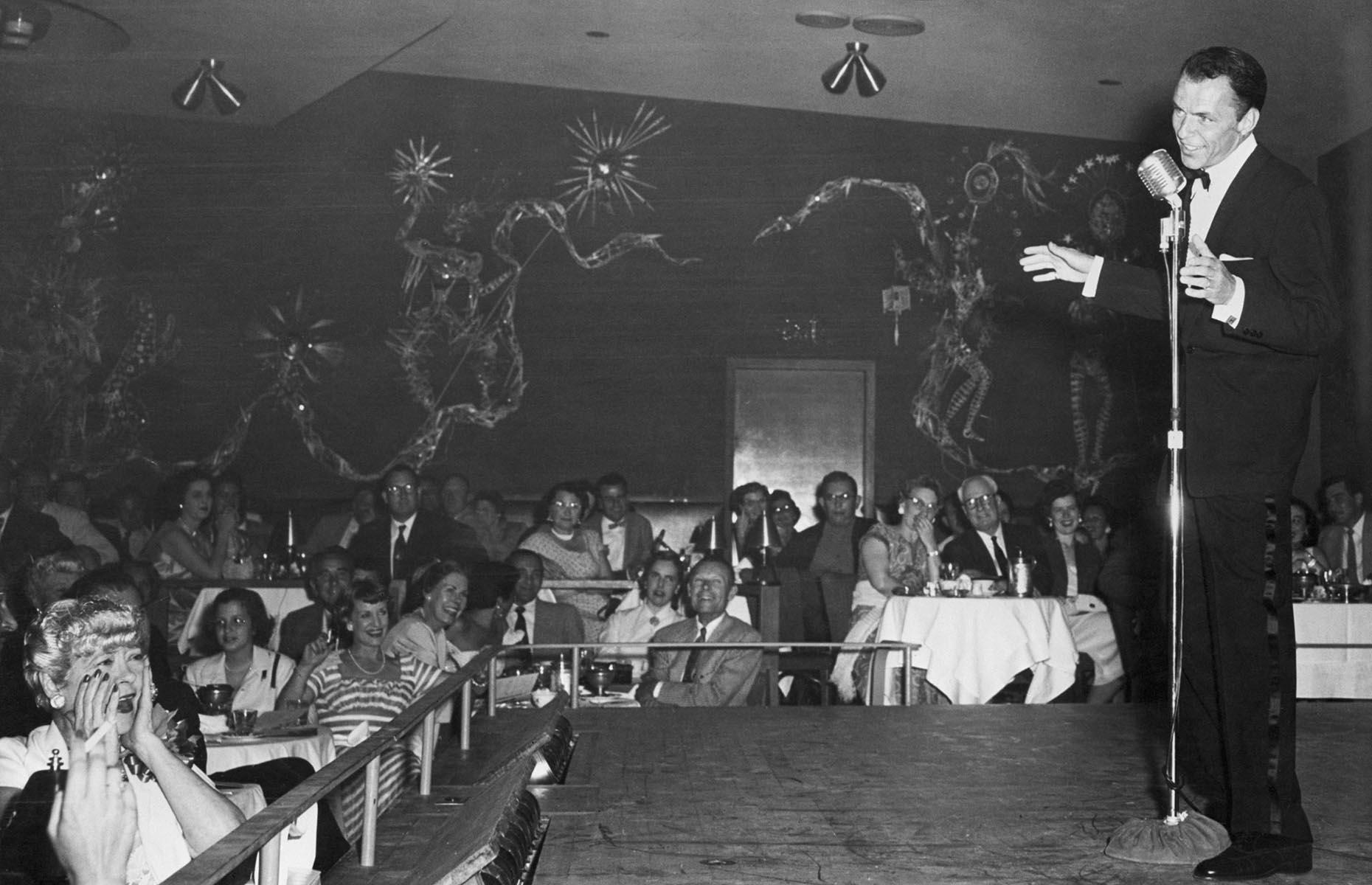 Slide 18 of 34: Although entertainment had been flourishing in Las Vegas for some time, none had quite left the mark that Frank Sinatra was about to. First appearing on stage in 1953 at the Sands Hotel, Frank Sinatra (pictured here at the Sands in 1954) loved Las Vegas and Las Vegas loved him. Sinatra headlined some of the biggest stages in the city, along with fellow performers Dean Martin, Sammy Davis Jr, Joey Bishop and Peter Lawford who collectively became known as the Rat Pack. They would make frequent joint stage appearances as well as gamble, drink and eat all across the city.