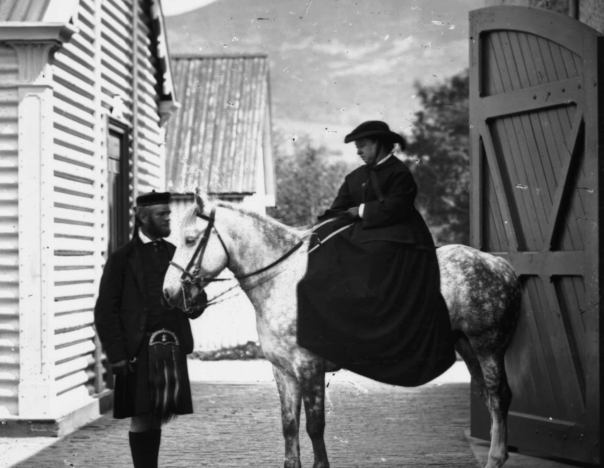 The Queen is snapped on a horse, ready for a ride at Balmoral. She’s accompanied by her personal assistant, John Brown.