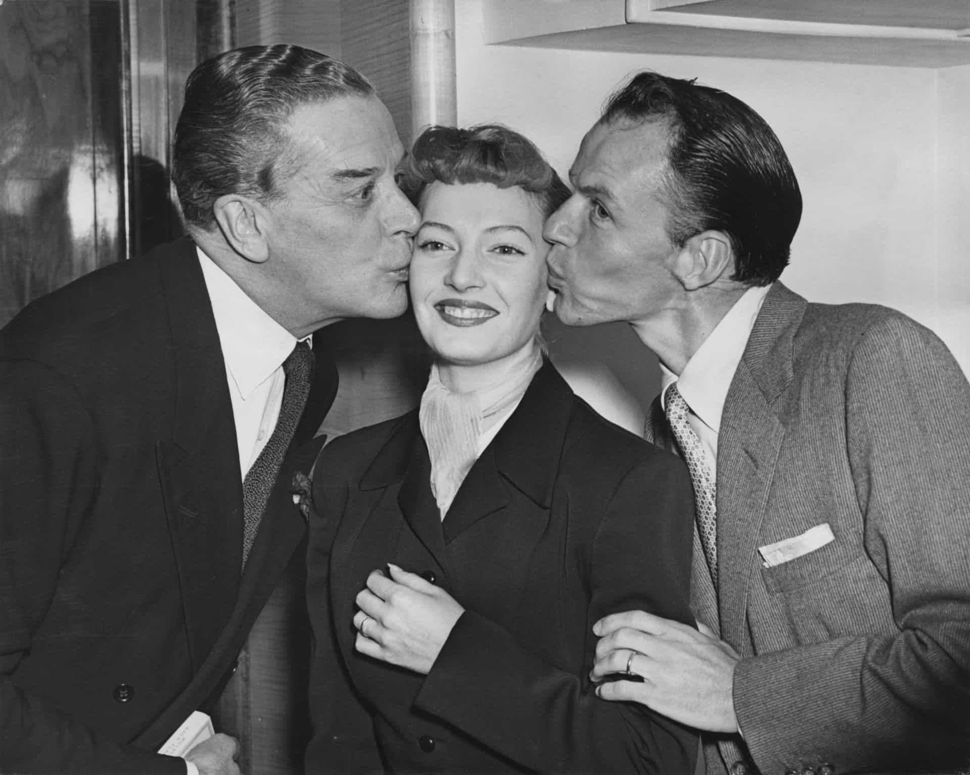 Sinatra (rechts) und der Schauspieler Jack Buchanan (links) küssen Schauspielerin Jeannie Carson während eines Variety Club Mittagessens im Savoy Hotel in London.