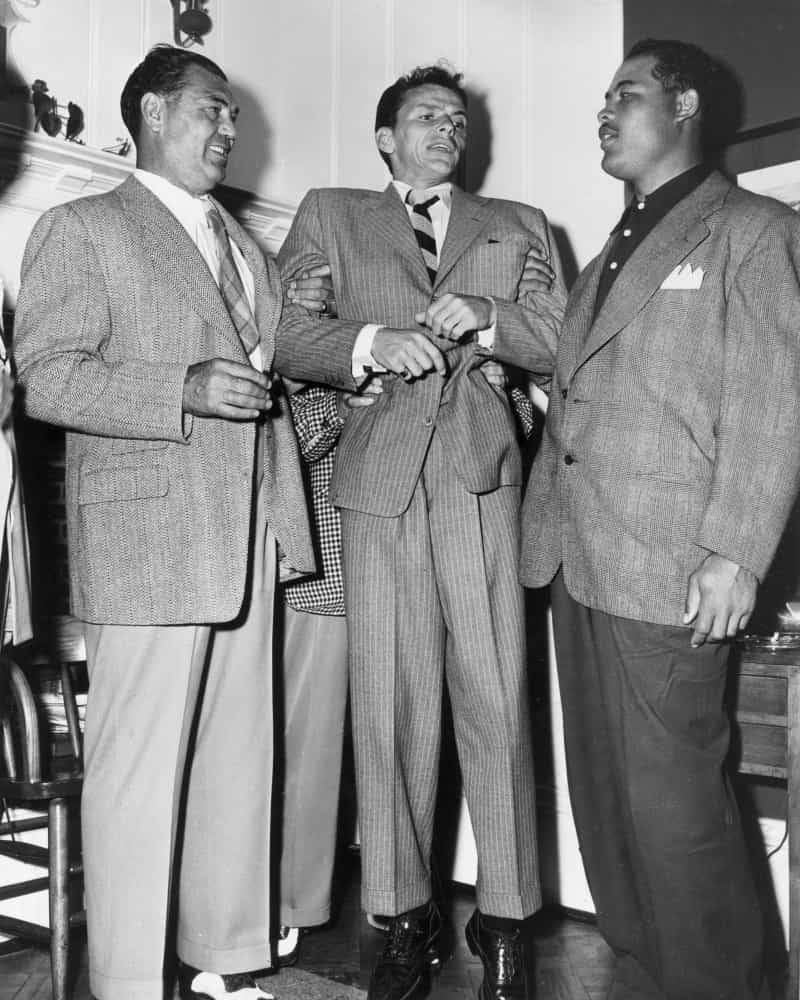Die Boxer Jack Dempsey (links) und Joe Louis (rechts) heben Frank Sinatra hoch.