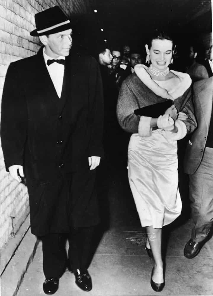 Sinatra, gekleidet in einem schwarzen Mantel, geht mit der amerikanischen Designerin und Erbin Gloria Vanderbilt spazieren.