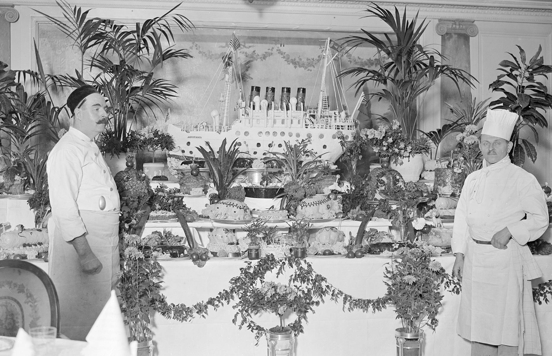 Huge dining rooms and bulging buffets are markers of the modern-day cruise and, in the 1920s, dinnertime was equally important. It was typically a grand affair requiring formal dress and involving course after course of fine food. Here, two chefs on Cunard's Aquitania stand before a splendid festive spread – the star is the giant cake in the shape of the ship.