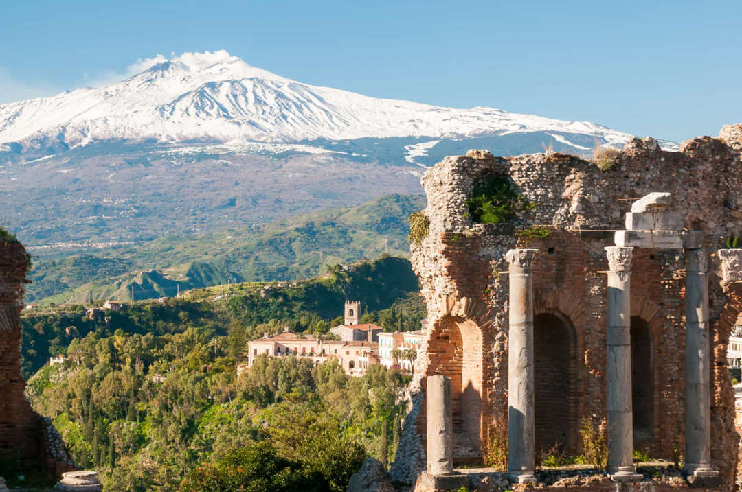 Slide 38 of 58: The ancient theater of Taormina, which dates back to the 3rd century BCE, is an island landmark. Mount Etna looms large in the distance.