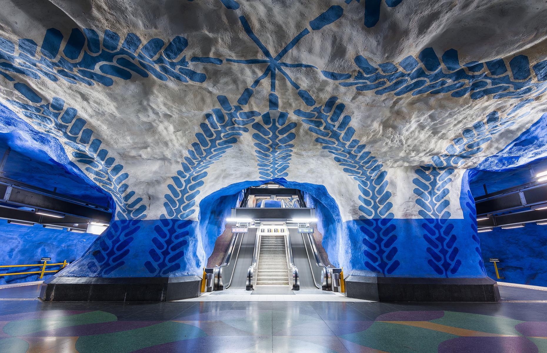Stockholm’s Centralen station, where all the metro lines converge, is perhaps the most recognizable of all. Blue vines climb up the white-washed grotto ceiling at platform level while red and green line platform walls above are decorated with colorful glass tiles.