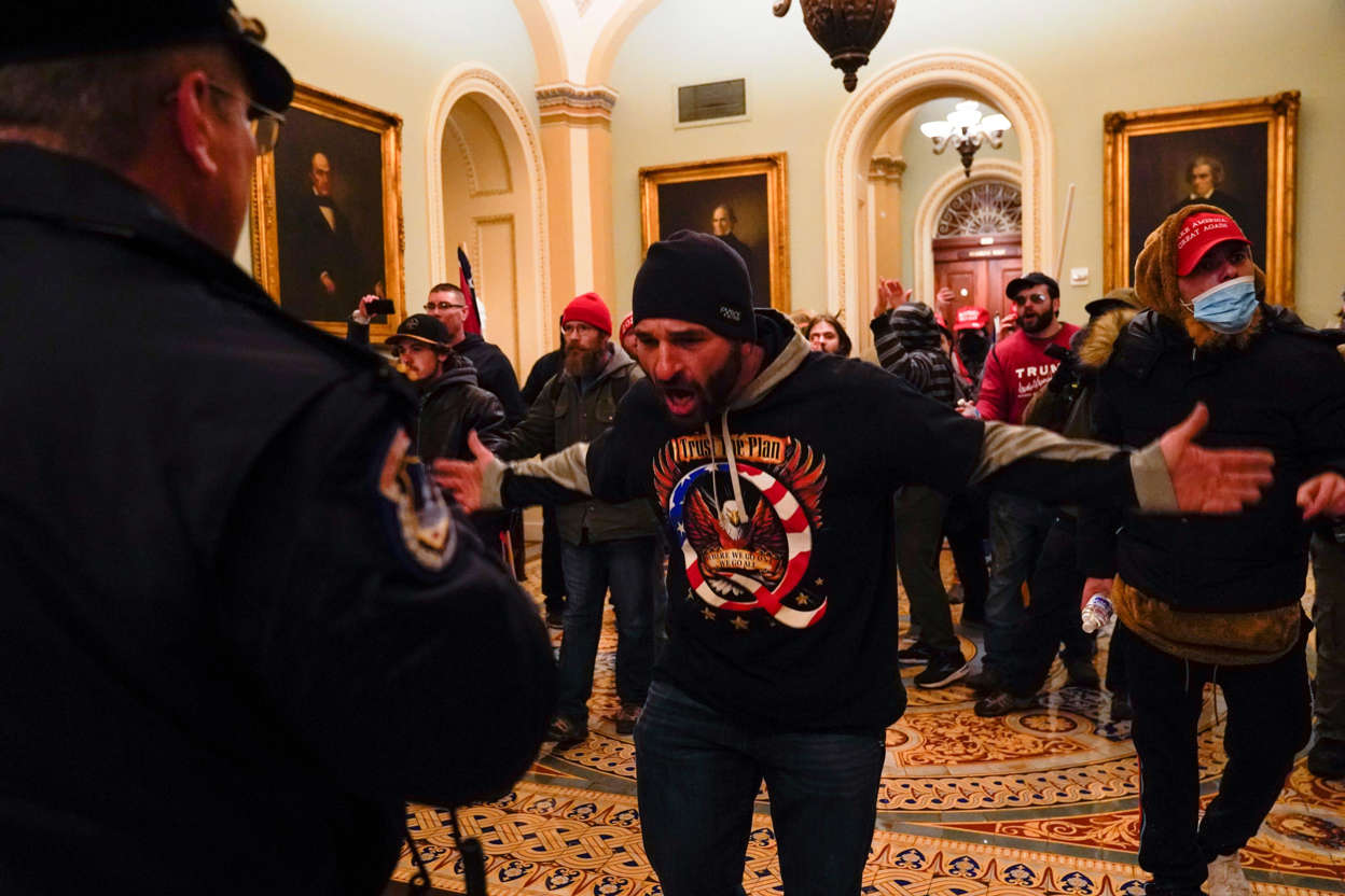 Slide 38 of 76: Protesters gesture to U.S. Capitol Police in the hallway outside of the Senate chamber at the Capitol in Washington, Wednesday, Jan. 6, 2021, near the Ohio Clock. At center is Doug Jensen of Des Moines, Iowa who was later arrested and charged, the Des Moines Register reported.