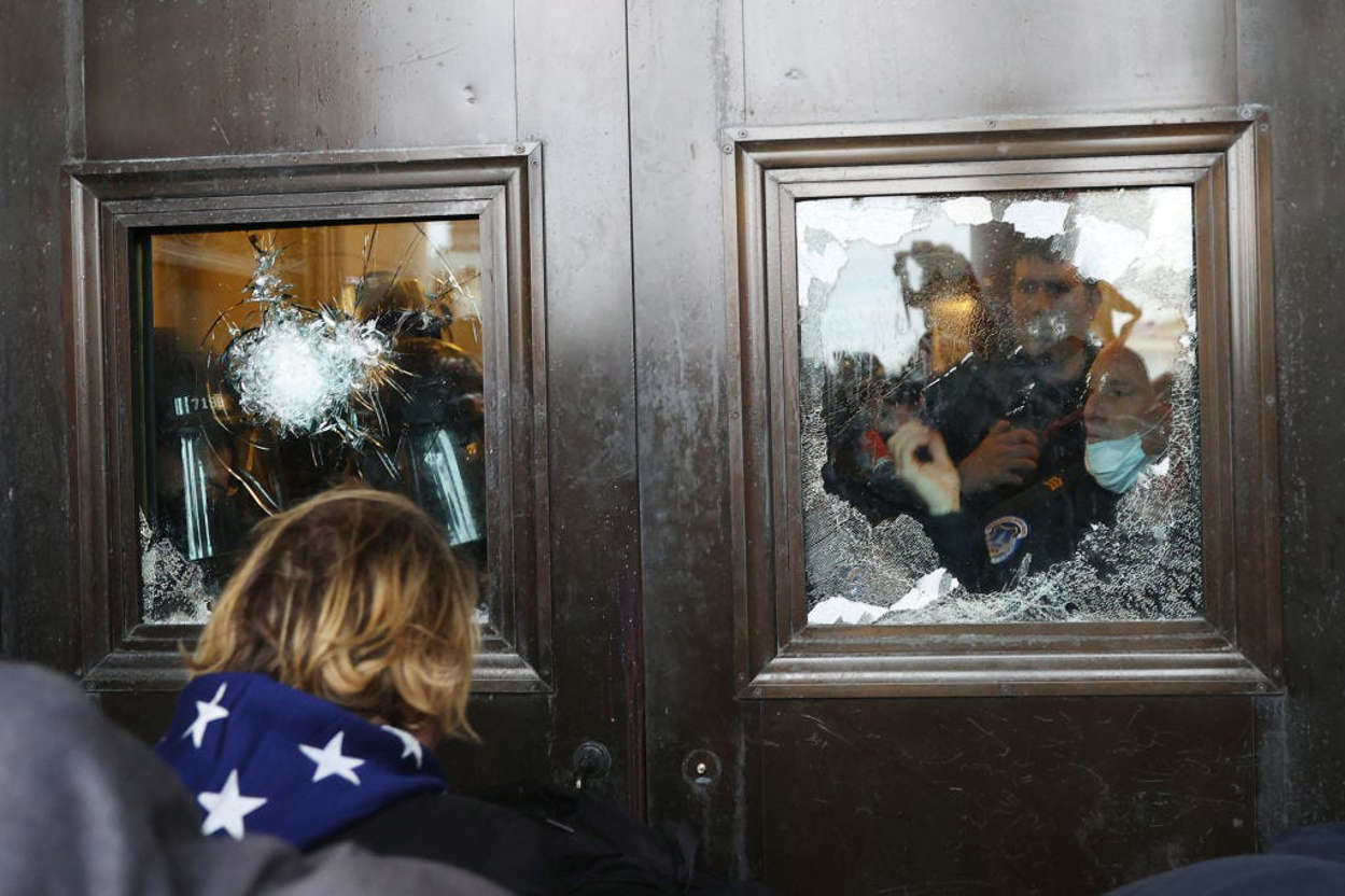 Slide 3 of 76: A Capitol police officer looks out of a broken window as pro-Trump rioters gather on the U.S. Capitol Building on January 06, 2021 in Washington, DC.