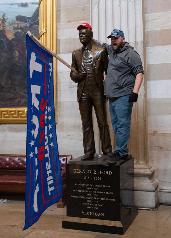 Slide 9 of 76: A protester adorns a statue of President Gerald Ford with Trump paraphernalia.