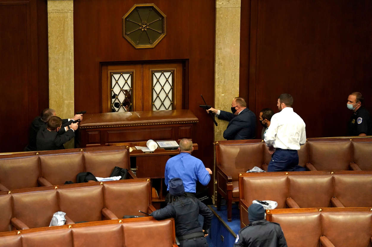 Slide 20 of 76: Law enforcement officers point their guns at a door that was vandalized in the House Chamber during a joint session of Congress on Jan. 06, 2021 in Washington, DC. Congress held a joint session today to ratify President-elect Joe Biden's 306-232 Electoral College win over President Donald Trump. A group of Republican senators said they would reject the Electoral College votes of several states unless Congress appointed a commission to audit the election results.