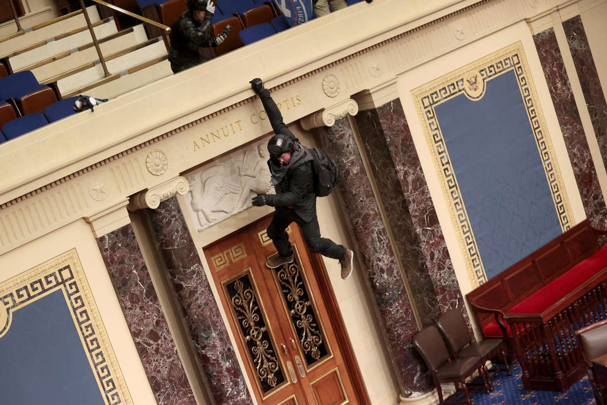 Slide 11 of 76: Pro-Trump rioter Josiah Colt is seen hanging from the balcony in the Senate Chamber on Jan. 6, 2021 in Washington, DC. Josiah Colt turned himself in at the Ada County Sheriff's Office in Boise, Idaho on Jan. 12, 2012.