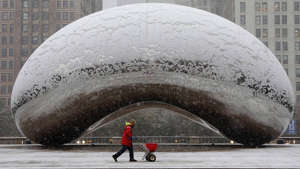 a person standing in front of Millennium Park: A maintenance worker spreads salt in the area around Cloud Gate during a morning rush hour snow storm as a winter weather advisory is issued for the Chicago area on Monday, Nov. 11, 2019. (Antonio Perez/ Chicago Tribune/Tribune News Service via Getty Images)