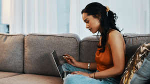 a woman sitting on a couch using a laptop: Saving up pays off