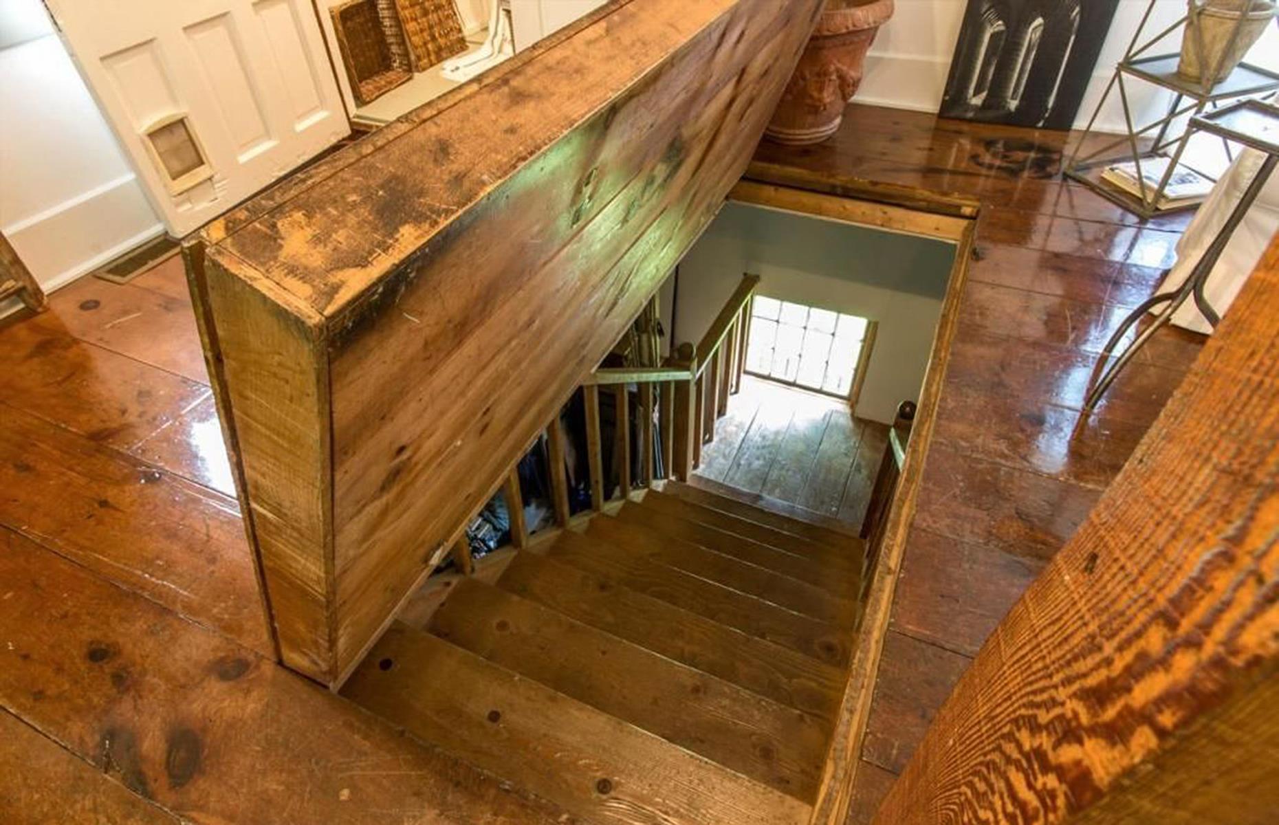 <p>The hatch is secured by a rope to a racket on the wall to reveal an old wooden staircase, leading down to the lower floor of this 1856 grist mill. Cover it up with a rug and you’d never even know it was there! </p>