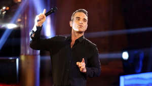 Robbie Williams standing on a stage: Take That had a constant chart presence in the 90s, with almost every album and song topping the UK charts.  However, in 1995, Robbie decided he did not want to be in Gary Barlow's shadow any longer and quit the boy band. He went on to achieve seven UK number one singles, twelve studio albums with six of his albums being among the top 100 biggest-selling albums in the UK, and in 2006 he entered the Guinness Book of World Records for selling 1.6 million tickets of his Close Encounters Tour in a single day.