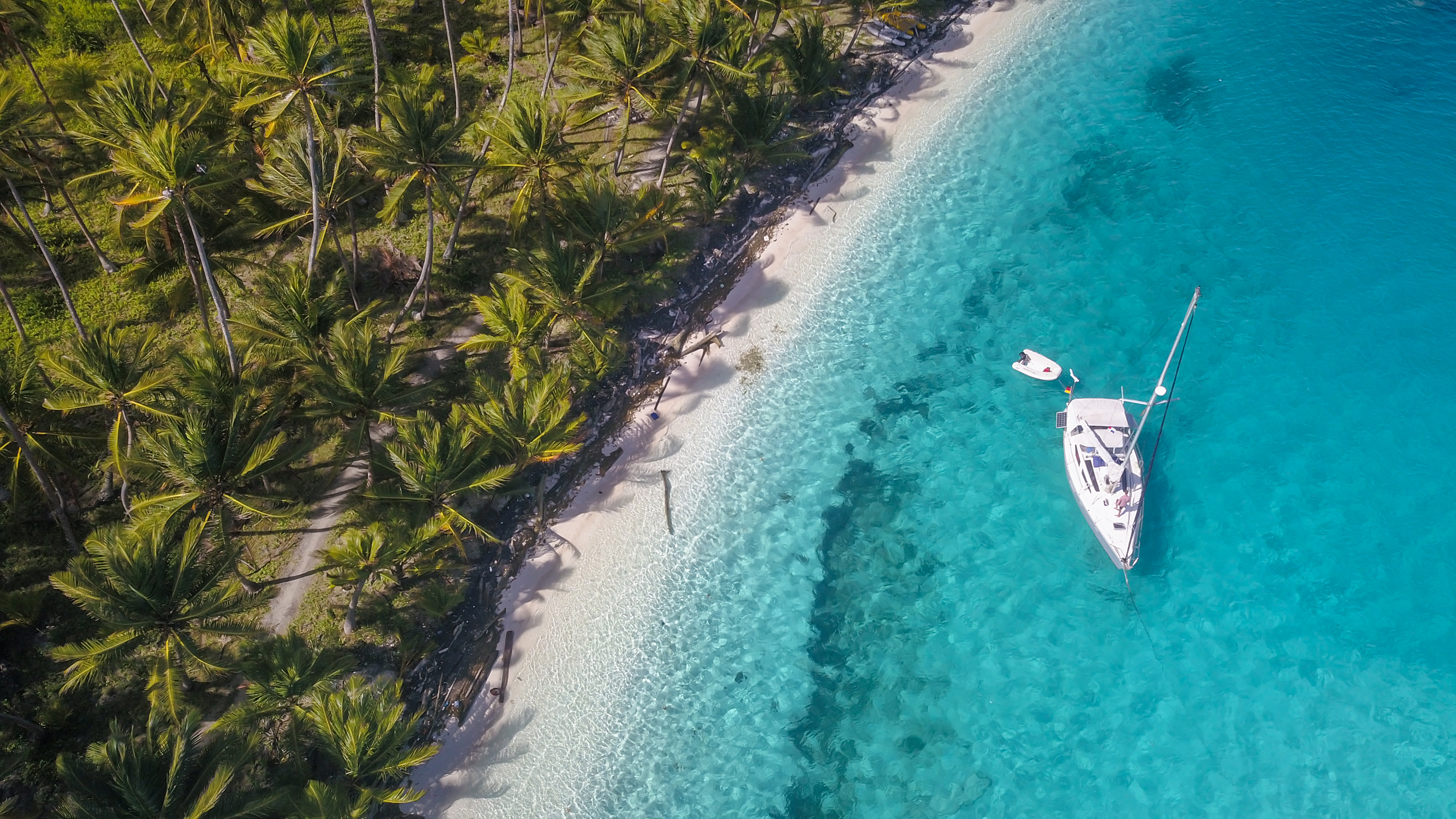 Slide 2 of 41: A beautiful Drone Shot of a white Sailing Yacht anchored in crystal clear Turquoise Water right next to the perfect White Sand Beach of a Tropical Island in the Caribbean San Blas Islands of Panama.