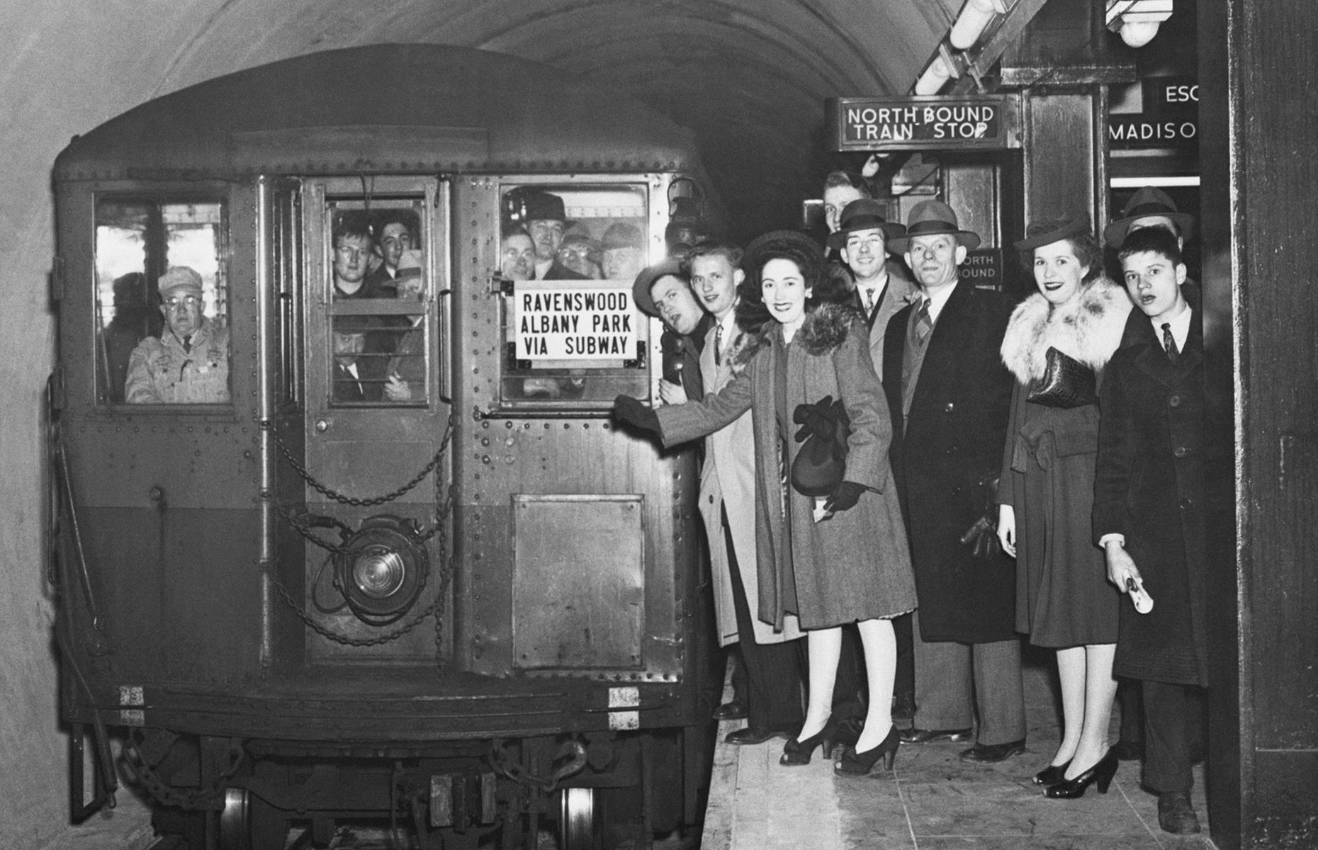 This photo shows a landmark day for Chicago's new subway system as the first paying passengers embark on a trip. Smiling Chicagoans look out from the platform and the crowded train, en route to Ravenswood and Albany Park, in October 1943.