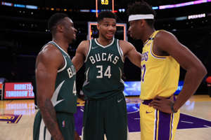 Giannis Antetokounmpo et al. standing on a court: Thanasis Antetokounmpo, Giannis Antetokounmpo and Kostas Antetokounmpo (from left to right) talk after the Milwaukee Bucks beat the Los Angeles Lakers on March 31, 2020 at STAPLES Center. It was the first time the three brothers played together in the NBA.