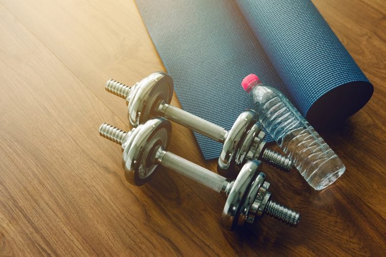 Pair of dumbbells with blue yoga mat on wood floor,flare light