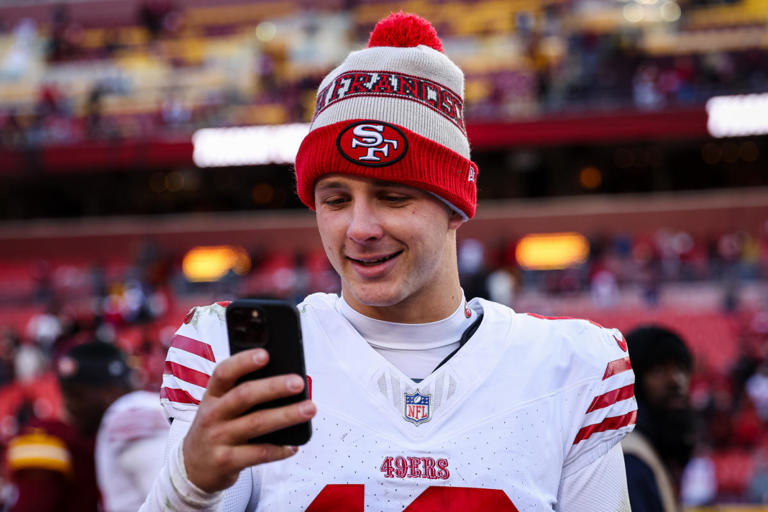 Brock Purdy #13 of the San Francisco 49ers interacts with a cellphone on the field after the game against the Washington Commanders at FedExField on December 31, 2023 in Landover, Maryland.  / Credit: Scott Taetsch/Getty Images