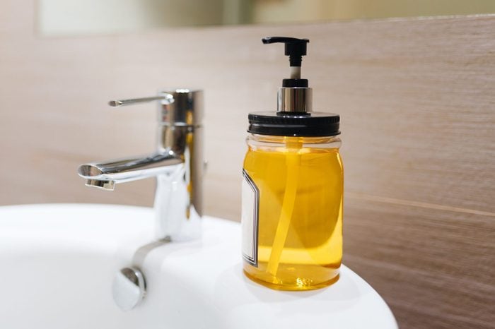 Close Up View Of A Bottle Of Yellow Hand Soap Next To A Bathroom Faucet. Organic Hand Sanitiser