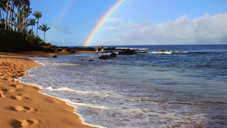 'Aloha' on Hawaiian beach beneath a rainbow.
