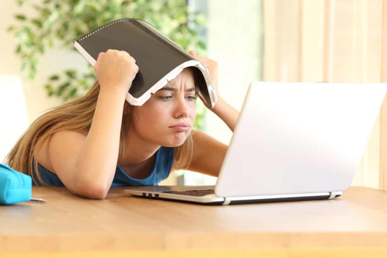 A girl using a laptop to work and complete tasks, while holding her head up.