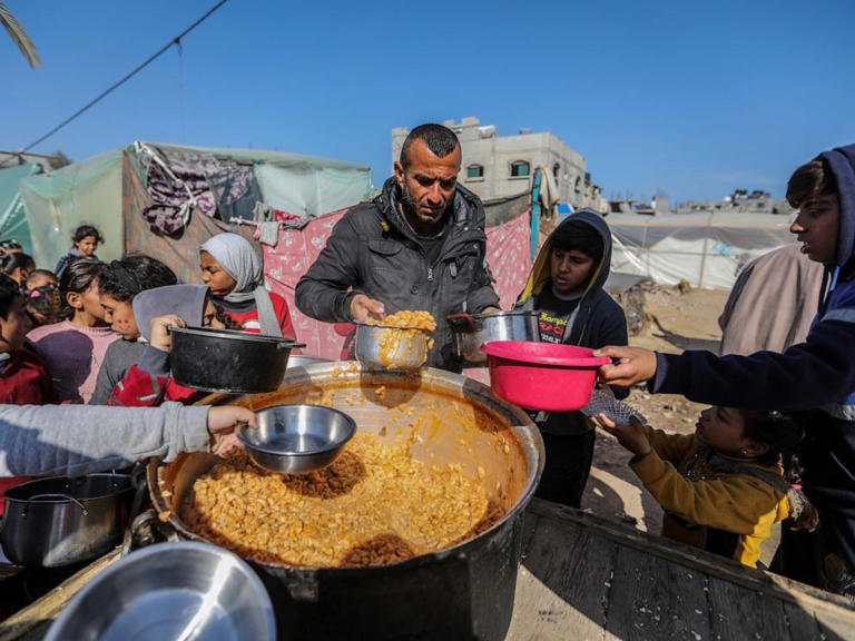 Displaced people line up to receive food near the tents in which they live, Jan. 20, 2024, in Rafah, Gaza.