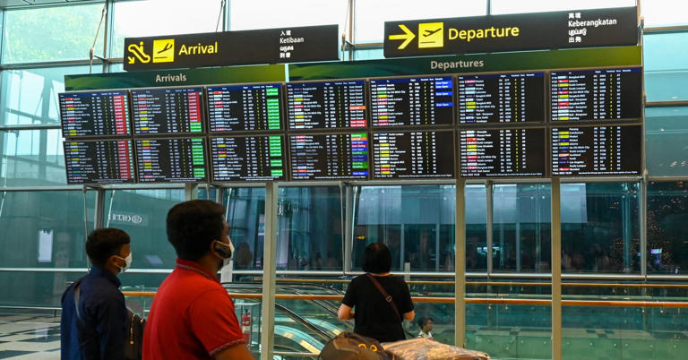 Travellers look at the flight departure schedule on the screen at Singapore Changi airport on December 7, 2022. 