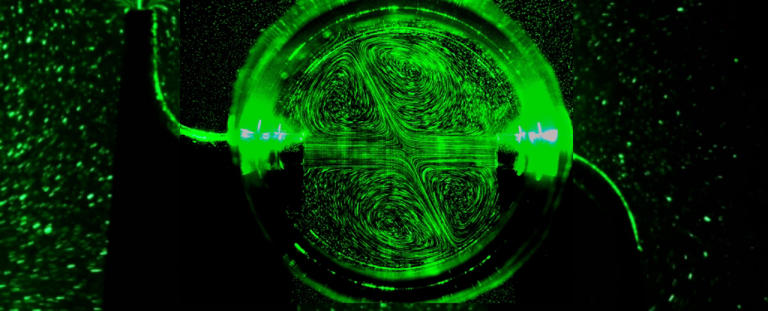 Close up of sprinkler hub and outflowing water jets, illuminated by green lasers.