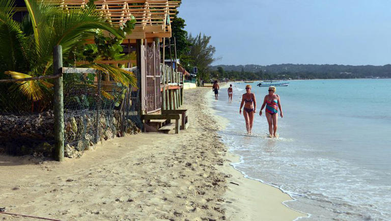 Sunbathers walk along a badly eroding patch of resort-lined crescent beach in Negril in western Jamaica in this 2014 file photo.