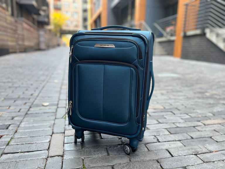 Samsonite SoLyte DLX Carry-On Spinner in blue in an alley.