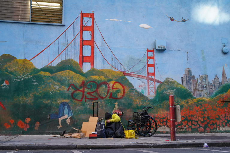 A homeless person lies against a mural of the Golden Gate Bridge near APEC Summit headquarters on Nov. 11, 2023, in downtown San Francisco.