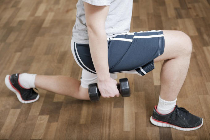 Knee physiotherapy. Male patient performing lunges with weights as part of physiotherapy after knee surgery. The surgery took place nine months previously, and was performed to reconstruct the anterior cruciate ligament (ACL) in his knee and repair the joint meniscus. The ACL is one of the four major ligaments that hold the knee joint together. It joins the femur (thigh bone) to the tibia (shin bone) and is commonly injured while playing sport.