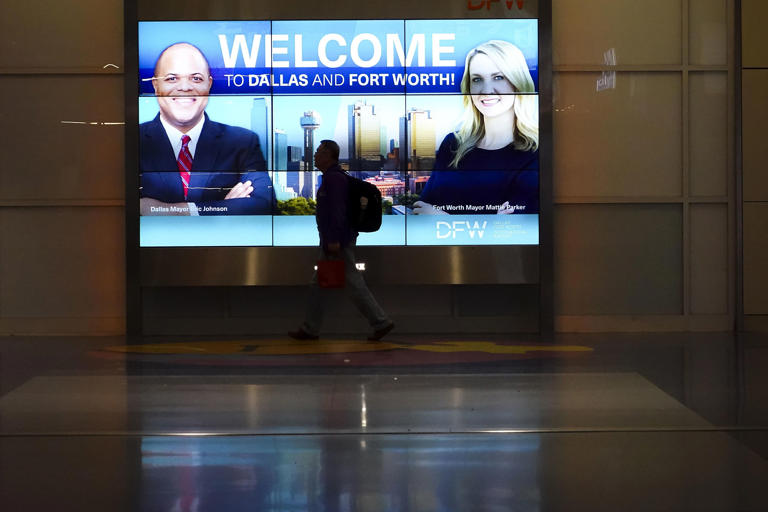 Passengers walk between gates of Terminal A past a display with images of Dallas Mayor Eric Johnson and Fort Worth Mayor Mattie Parker at DFW Airport on Saturday, Feb. 3, 2024.