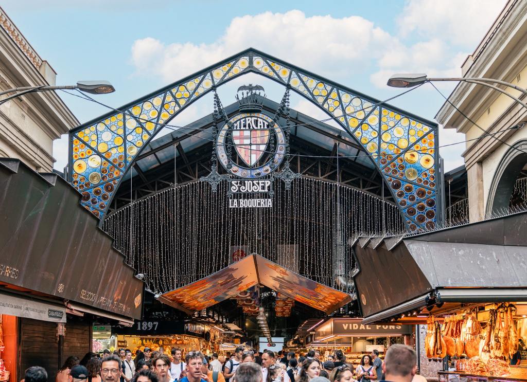 <p>Discover the lively Mercat de Sant Josep de la Boqueria in <a href="https://worldwildschooling.com/barcelona-with-kids/">Barcelona</a>, renowned for its fresh produce and local delicacies. Absorb the lively atmosphere of this bustling marketplace as you sample a variety of fruits and specialties. Indulge in tapas, whether grabbing quick bites or unwinding at nearby bars.</p><p>From cones with calamari, serrano ham, and cheese to flavorful empanadas and fresh fruit, exploring this market is among our top recommendations for experiencing Barcelona’s gastronomy.</p><p class="has-text-align-center has-medium-font-size">Read also: <a href="https://worldwildschooling.com/small-towns-in-europe/">Most Charming European Towns</a></p>