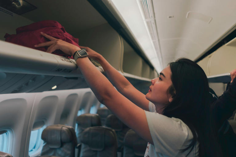 woman passenger in action of trying herself to prepare the bag luggages equips to storage on overhead locker compartment of the airplane, support or help require for woman traveler alone