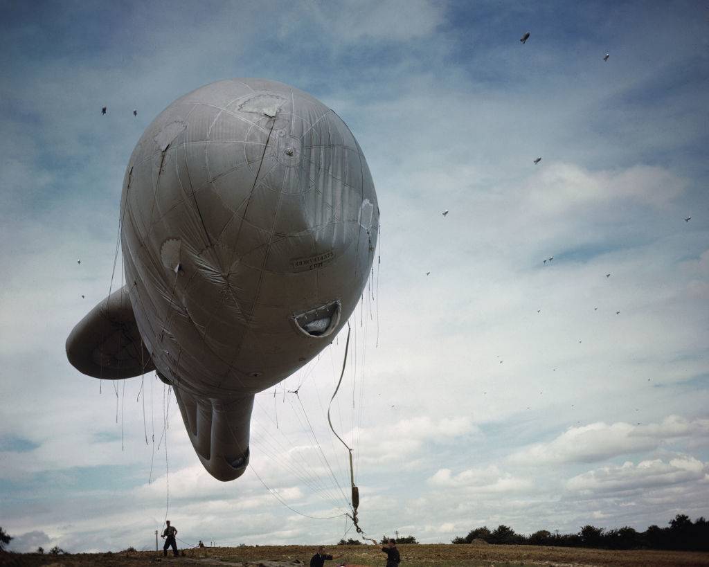 <p>A barrage balloon is a kite balloon that was utilized to defend ground targets against enemy aircraft. They were tethered to the ground using steel cables, which posed a major risk to aircraft that made an attempt to fly through them. </p> <p>Taken from the design of the initial kite balloon, this new shape meant that it could be operated even if there was wind, unlike the regular circular balloon. These were heavily used during World War II. </p>