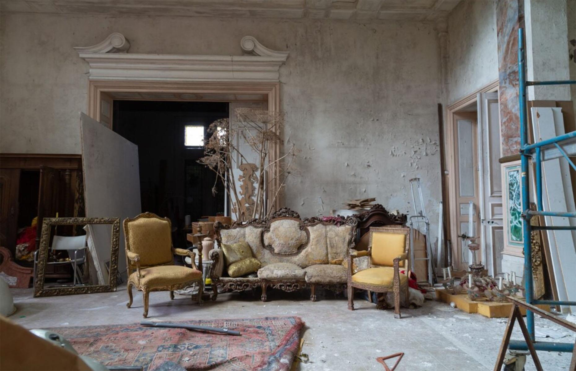 <p>This spacious room would likely once have been the heart of the home, with high ceilings and plenty of elegant seating.</p>  <p>While the plaster is peeling from the walls, there is still a sort of stripped-back elegance to this space, which throws the grandeur of the furniture and highly decorative door frames into even sharper relief.</p>