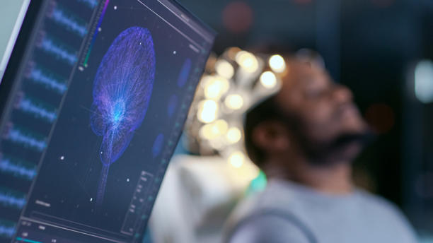 Monitors Show EEG Reading and Graphical Brain Model. In the Background Laboratory Man Wearing Brainwave Scanning Headset Sits in a Chair with Closed Eyes. In the Modern Brain Study Research Laboratory