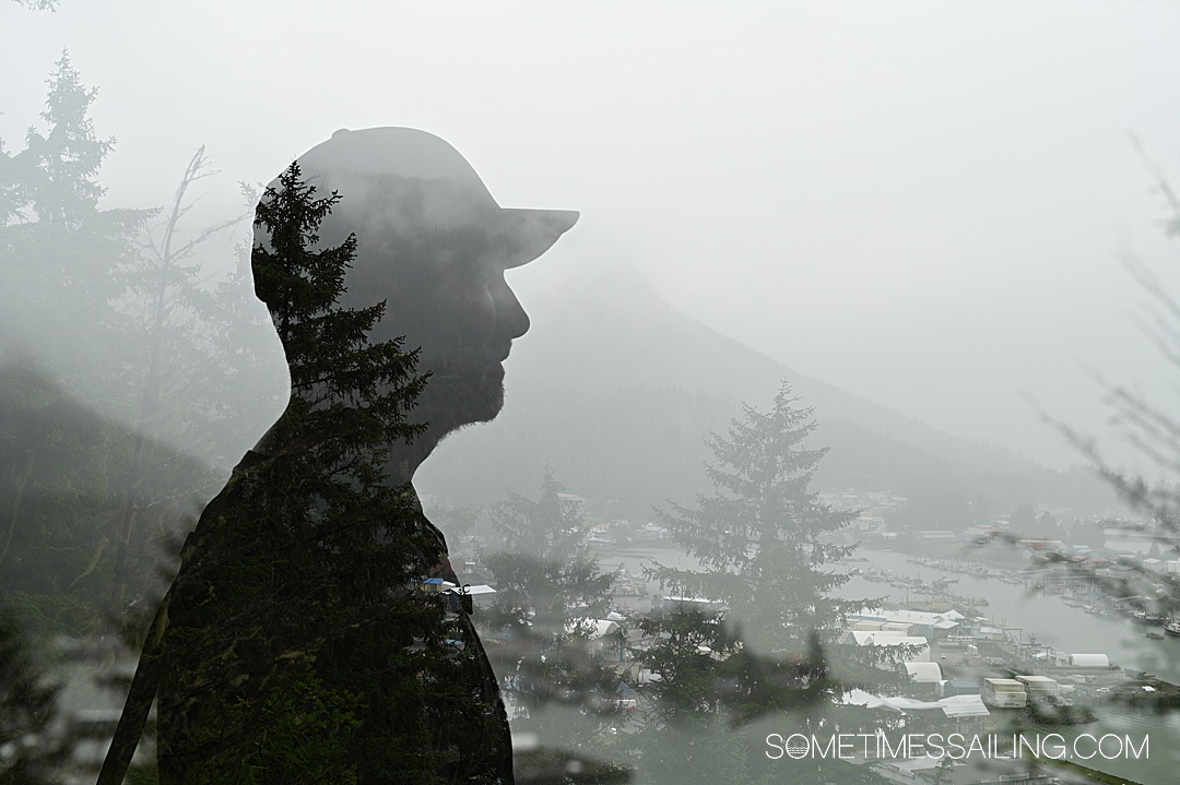 Double exposure photo with the silhouette of the profile of a man in a baseball cap with a landscape of evergreens and a harbor in Wrangell, Alaska.