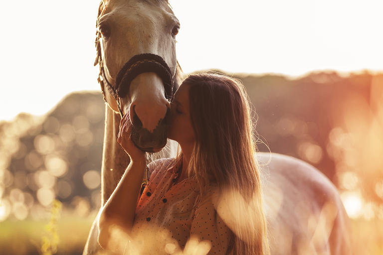 Woman kissing her horse at sunset
