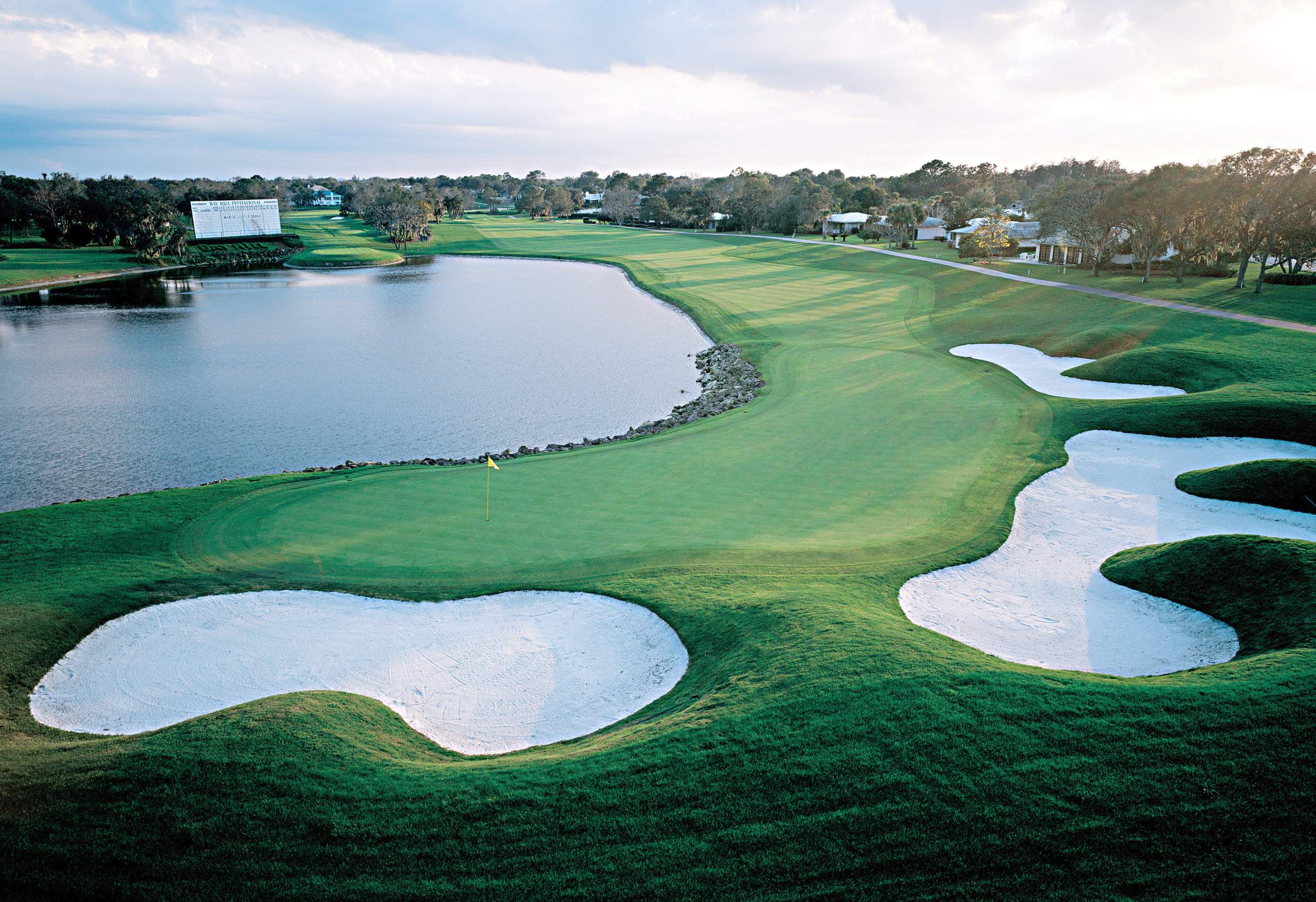 <em><b>Course Location: Orlando, Florida</b></em> The Bay Hill Club & Lodge stands as a bastion of exclusive golfing and hospitality nestled in the sun-kissed landscapes of Bay Hill, Florida, a serene suburb southwest of Orlando. Crafted under the meticulous eye of renowned architect Dick Wilson in 1961, the initial 18 holes, known as the Champion and Challenger nines, epitomize Wilson's ingenuity, boasting subtly elevated greens enhancing both visibility and drainage. Following Wilson's legacy, the additional nine holes, named the Charger Nine, were masterfully fashioned by Bob Simmons. From its inception in 1974 until the passing of its legendary proprietor, Arnold Palmer, in 2016, Bay Hill Club & Lodge bore the indelible stamp of Palmer's vision. Presently, under the stewardship of his daughter and son-in-law, Amy & Roy Saunders, the establishment continues to exude the essence of Palmer's legacy.