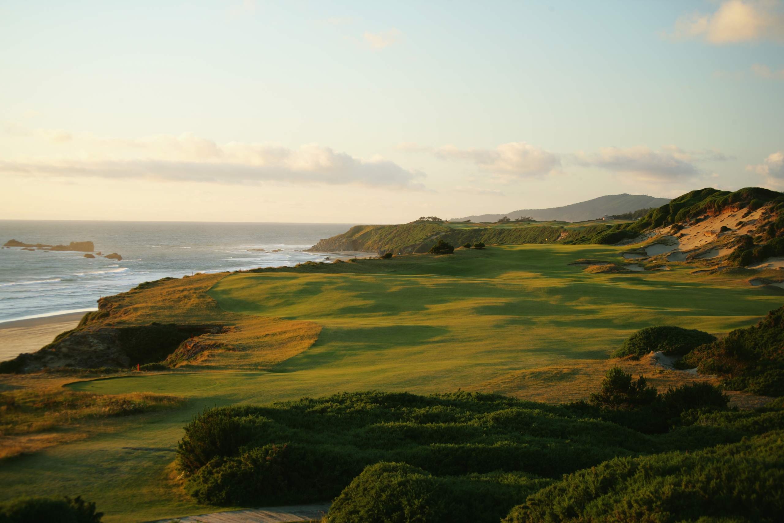 <em><b>Course Location: Bandon, Oregon</b></em> Crafted under the meticulous eye of renowned architect Tom Doak and unveiled in 2001, Pacific Dunes stands as a testament to the raw beauty of nature. Unlike its counterparts, Pacific Dunes doesn't feel like it was built as much as it was discovered. Its undulating fairways and untouched bunkers seamlessly blend into the coastal landscape, evoking a sense of timeless charm. The course emerges from shore pines to spectacular 60-foot sand dunes. The ever-present wind adds an element of challenge, demanding precision from every shot. Pacific Dunes is short enough to give you hope but rugged enough to test every facet of your game. You will be hard-pressed to find a more beautiful golf course.