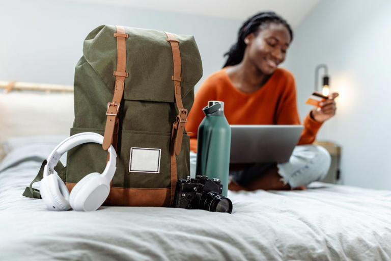 woman online shopping with travel accessories nearby