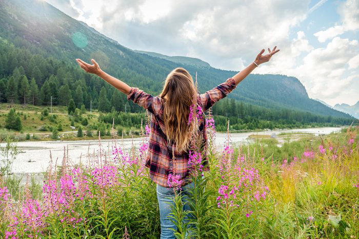 Cheering Woman Open Arms At Sunrise In Wild Flowers Field By The River